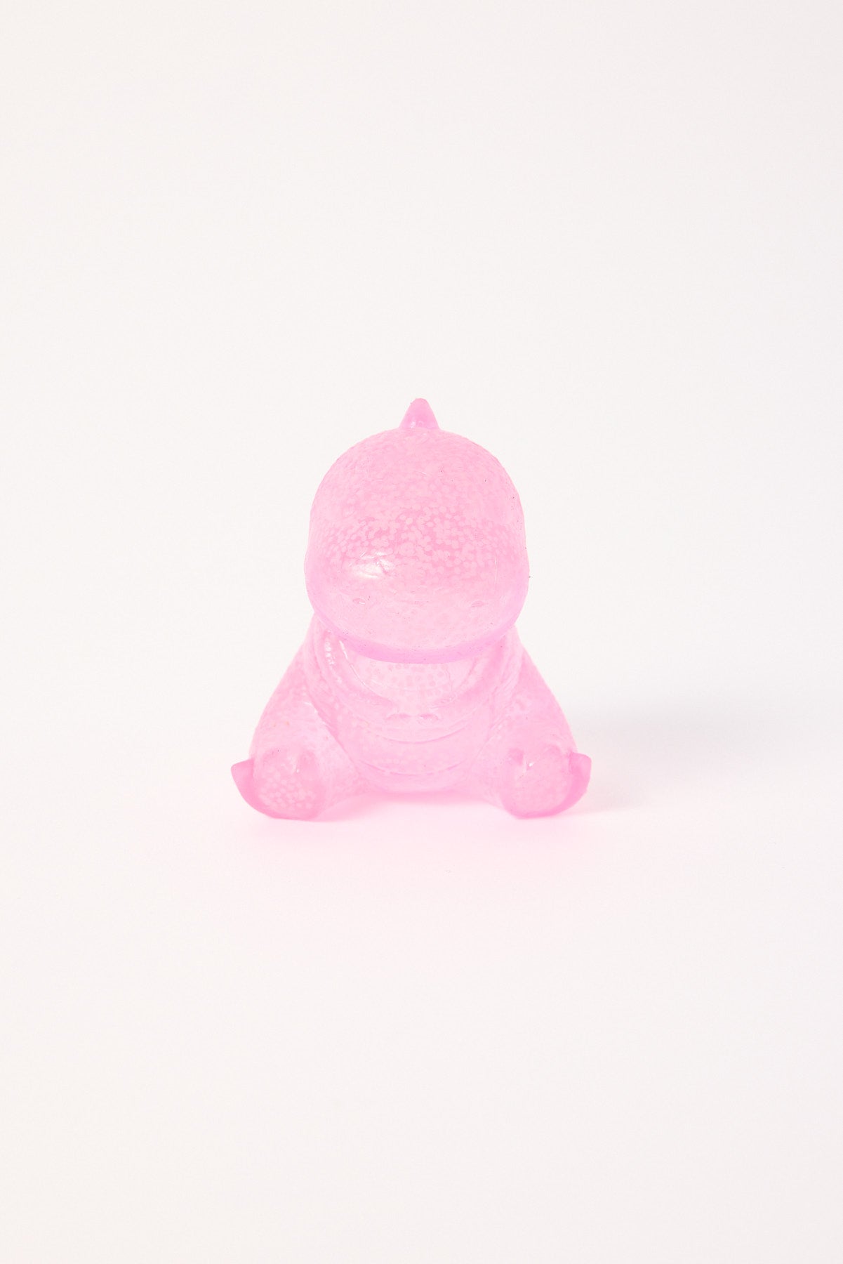 Translucent pink baby dinosaur toy sitting on a white surface