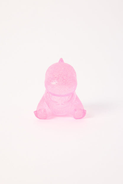 Translucent pink baby dinosaur toy sitting on a white surface