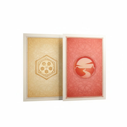 Two Gamegenic Catan Art Sleeves, one gold with a soccer ball-like emblem, the other red with a circular landscape and winding path