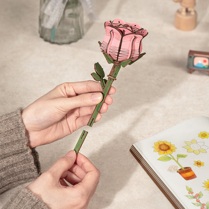 Hands connecting the stem pieces of a pink wooden rose 3D puzzle