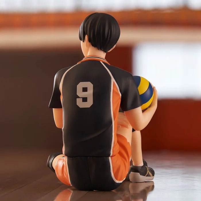 Figure of a male volleyball player in a black and orange jersey sitting on the floor holding a volleyball