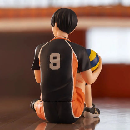 Figure of a male volleyball player in a black and orange jersey sitting on the floor holding a volleyball