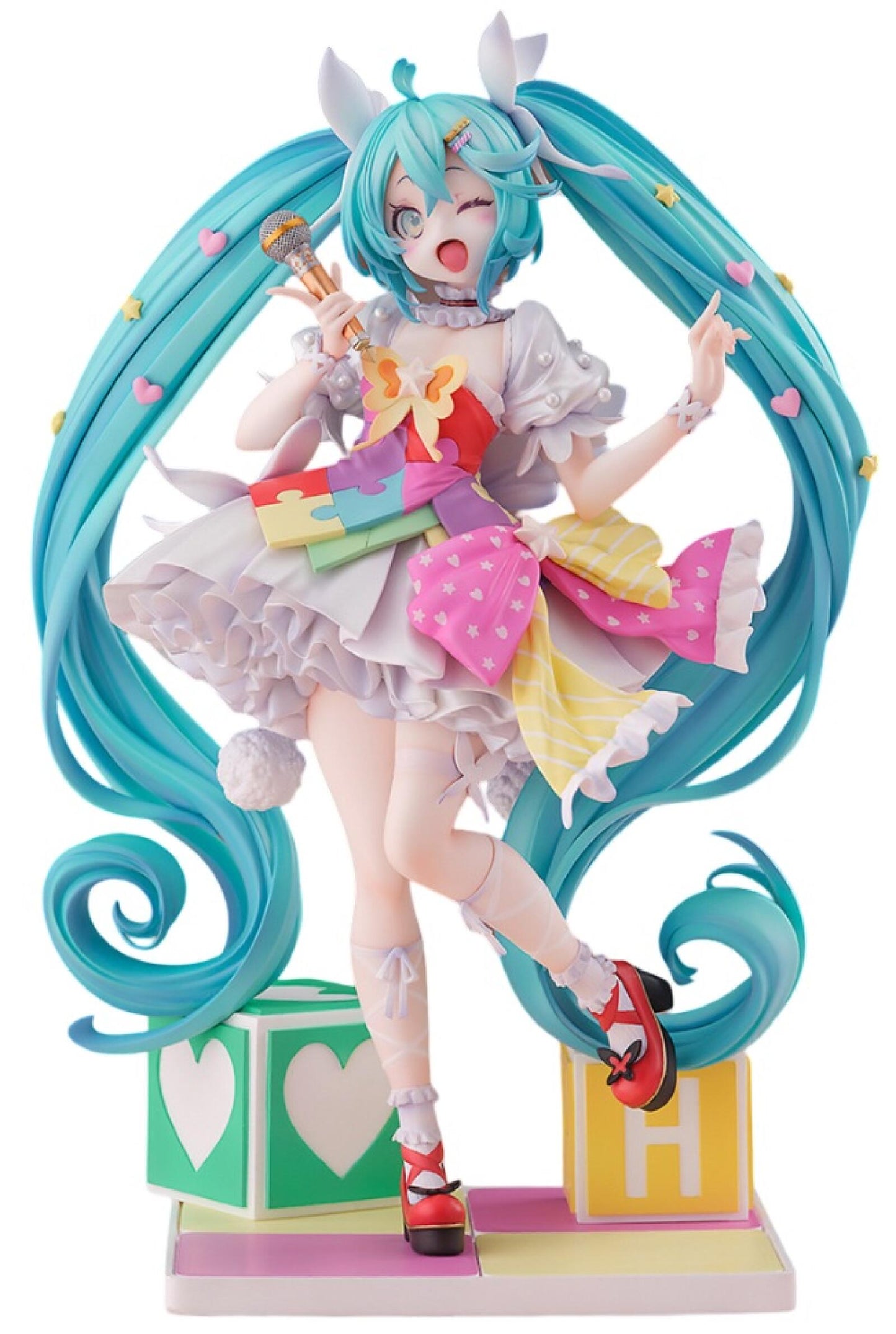 Hatsune Miku figure winks and sings into a mic- she wears a colorful puzzle dress, long teal pigtails, and stands on toy blocks