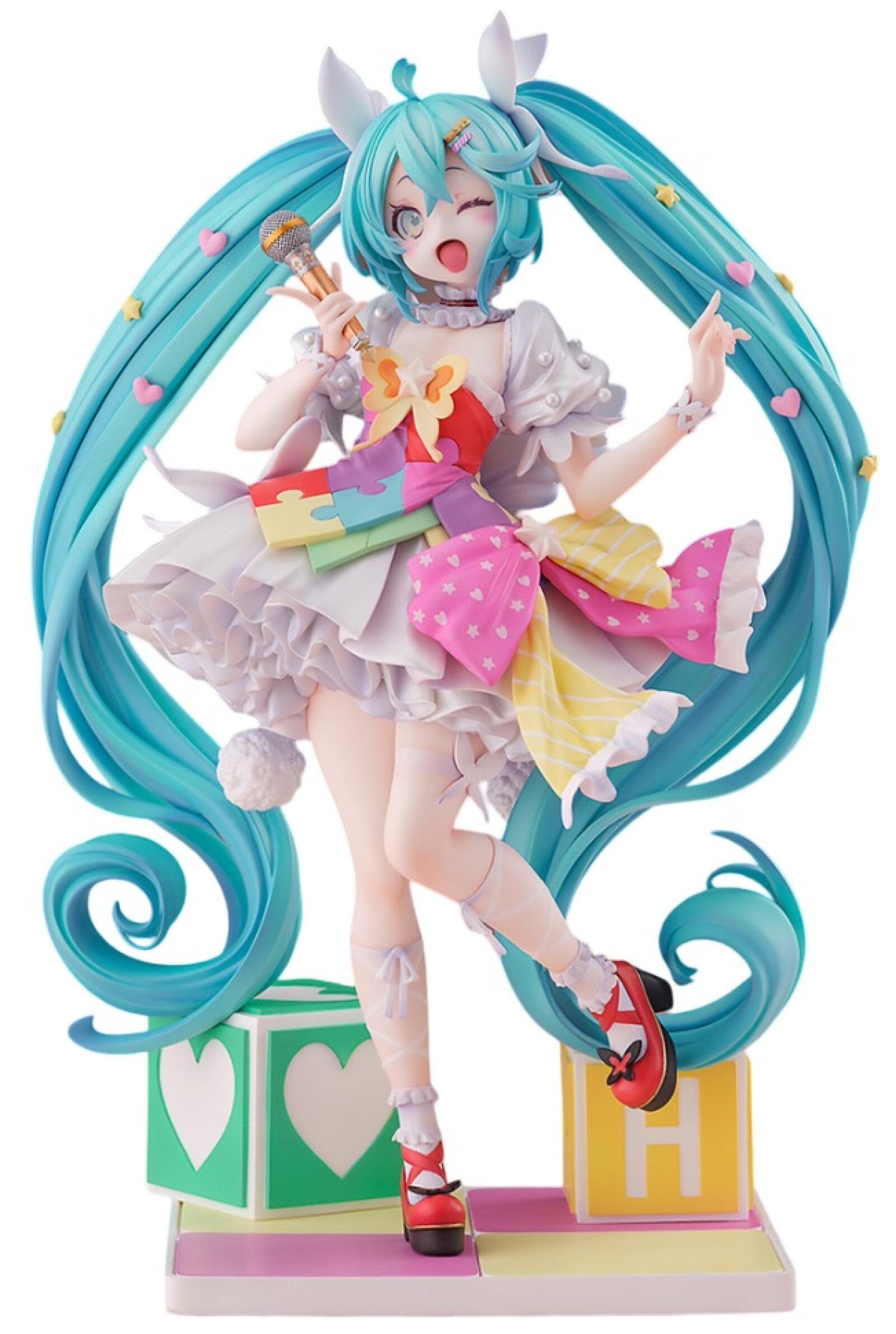 Hatsune Miku figure winks and sings into a mic- she wears a colorful puzzle dress, long teal pigtails, and stands on toy blocks