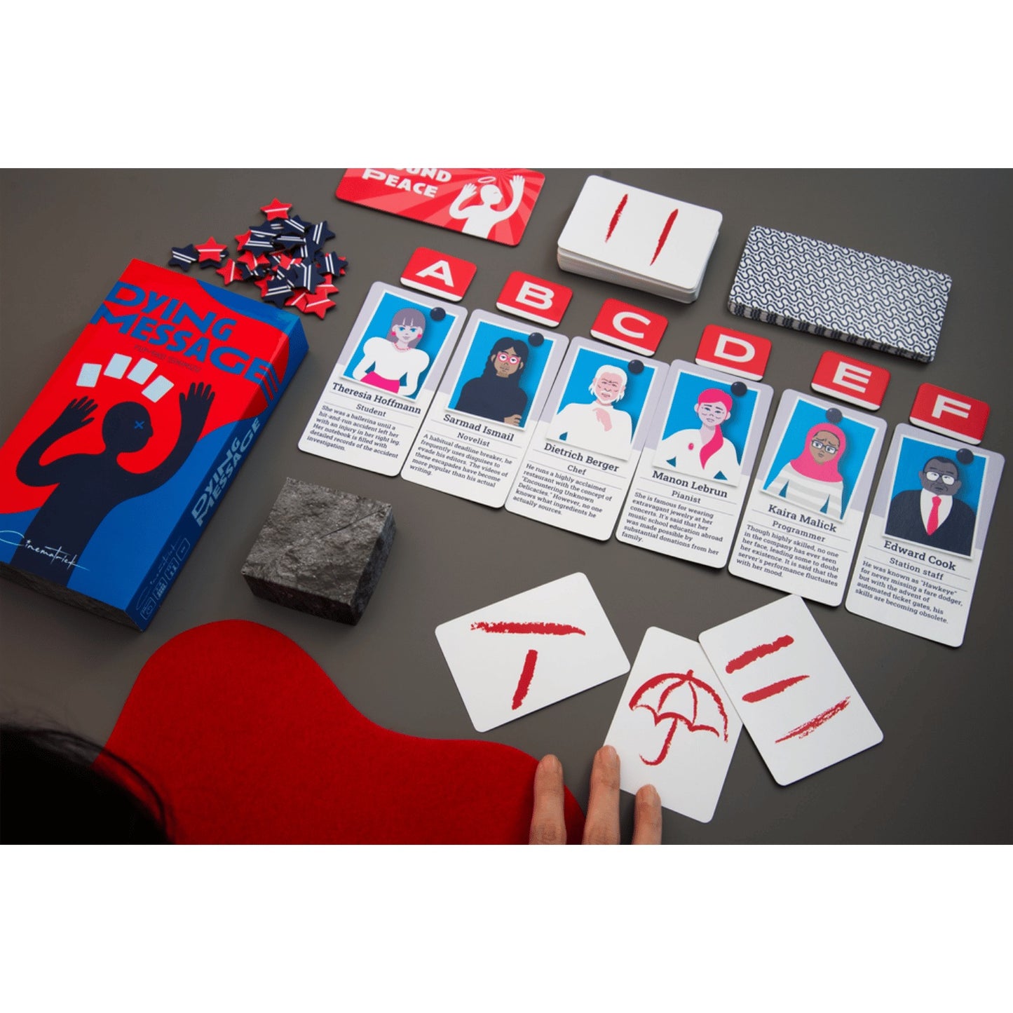 Oink Games Dying Message game components are displayed on a table with a hand touching symbol cards, surrounded by character cards and tokens
