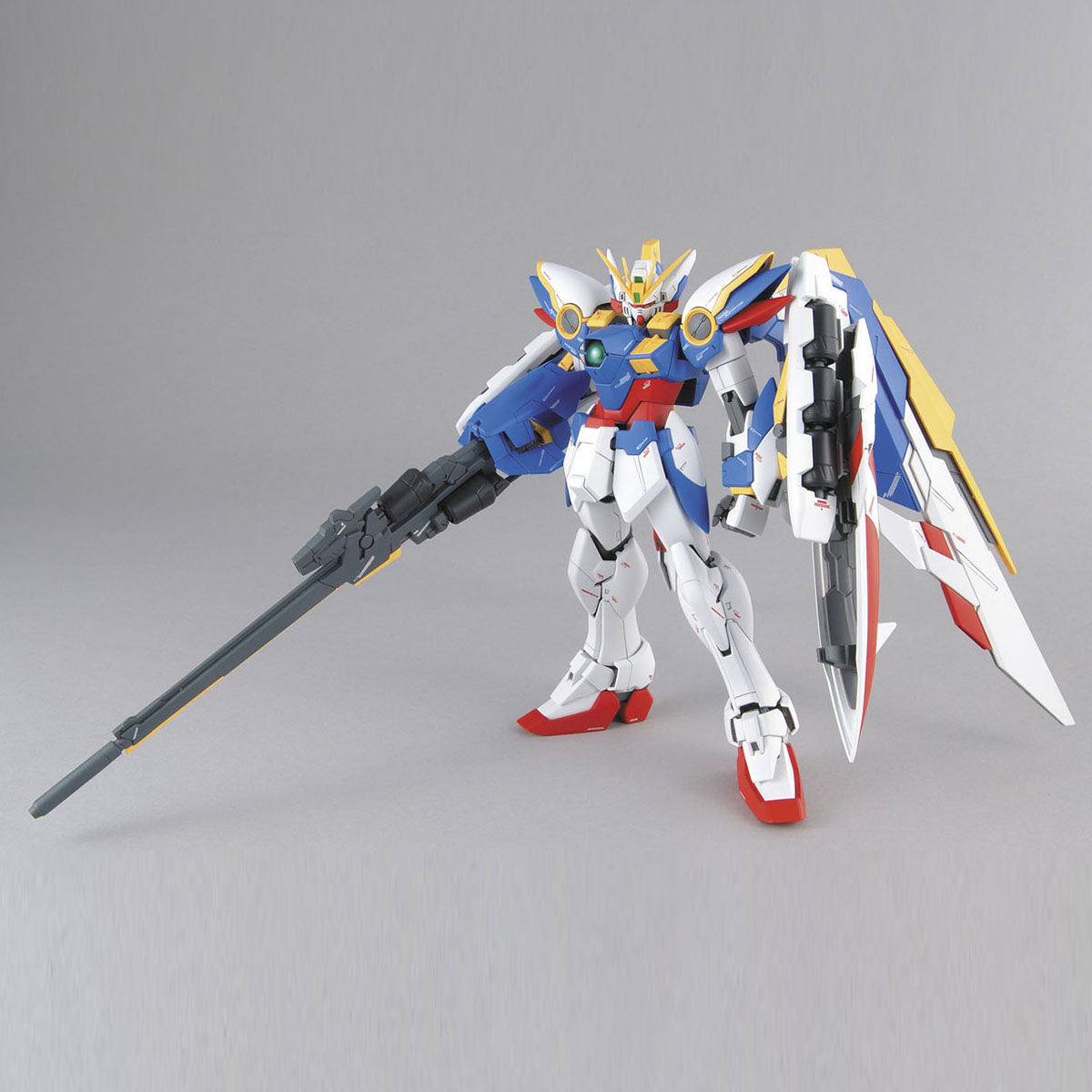 White and blue Wing Gundam model kit standing with large wings and holding a long rifle