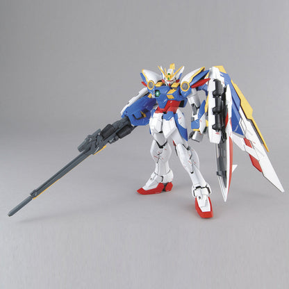 White and blue Wing Gundam model kit standing with large wings and holding a long rifle