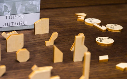 The Tokyo Jutaku game box stands behind various wooden building-shaped pieces and circular tokens scattered on a dark wooden surface
