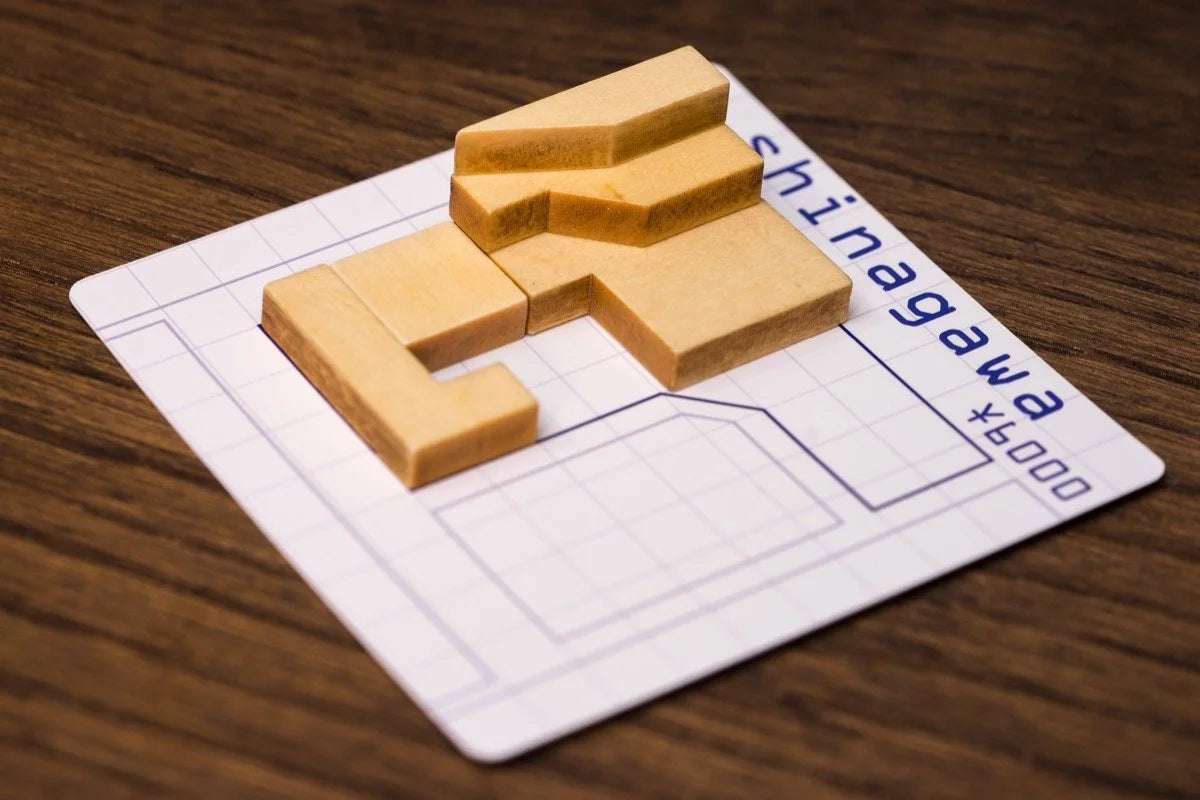 Wooden building-like puzzle pieces from Tokyo Jutaku are arranged on a grid card labeled Shinagawa