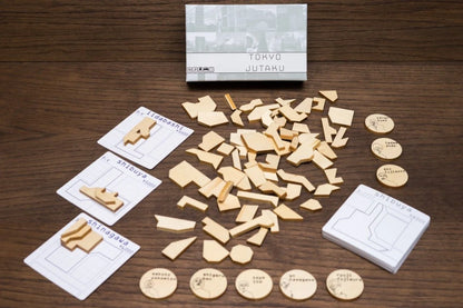 Tokyo Jutaku board game with its box, many small wooden geometric pieces, several cards, and round wooden tokens laid out on a wooden table