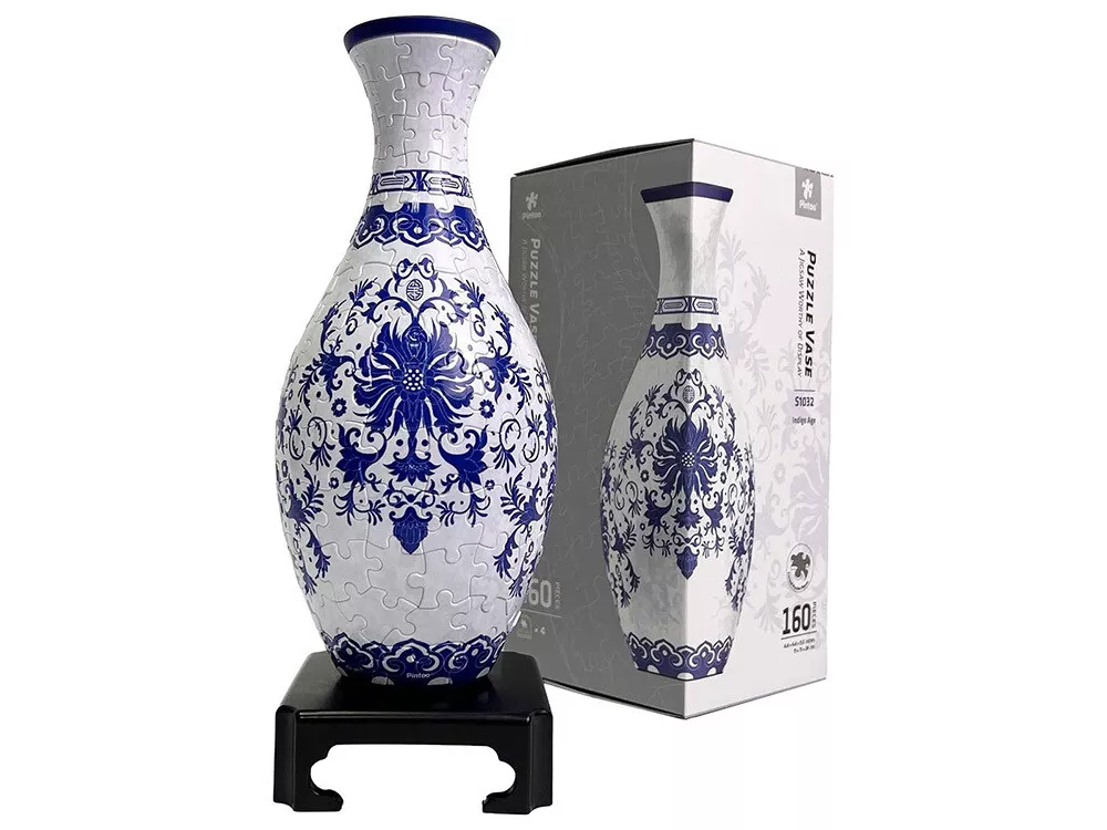 A 160-piece Puzzle Vase Indigo Age, fully assembled with blue and white porcelain-style patterns, sits on an ornate black stand with its box visible behind