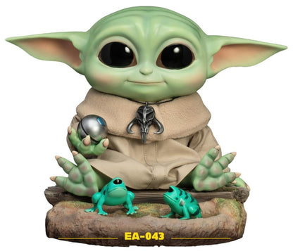 Grogu from Star Wars The Mandalorian figure holding a silver ball with two teal frogs on a log base