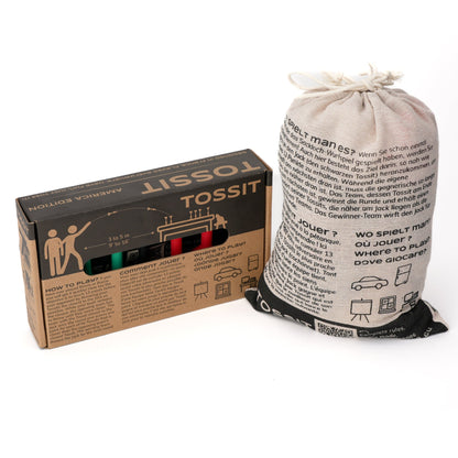 The Tossit Starter Pack America Edition box stands beside a tall, natural linen drawstring bag printed with multilingual rules