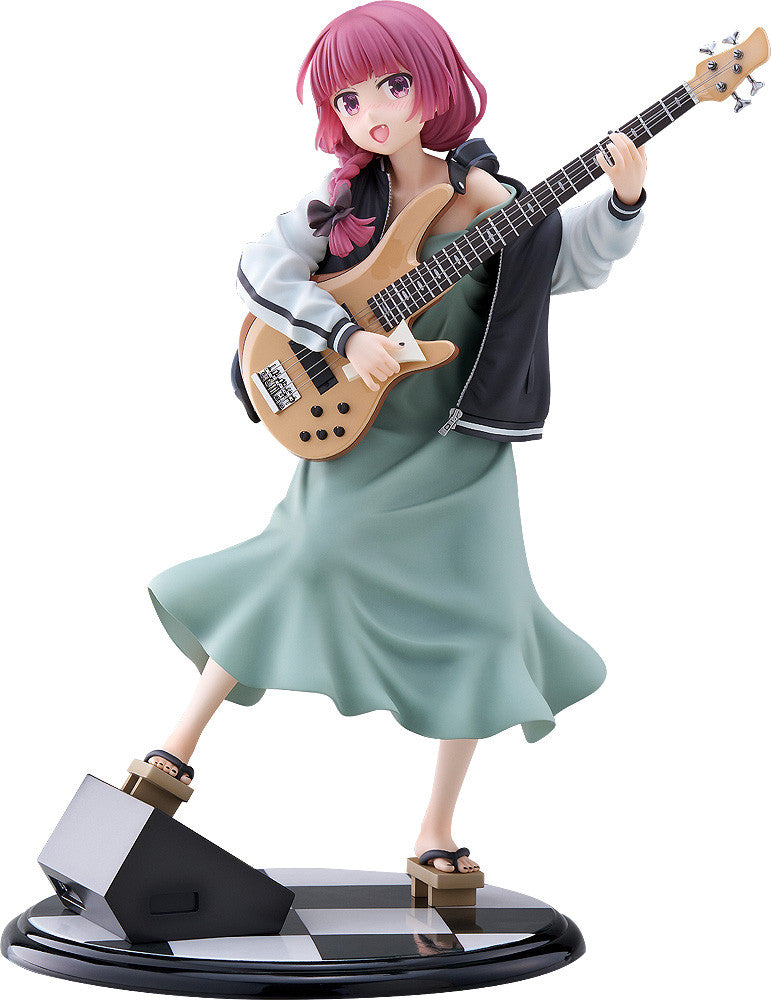 Pink-haired anime girl figurine in mint dress and jacket, energetically playing a bass guitar with one foot on a speaker base