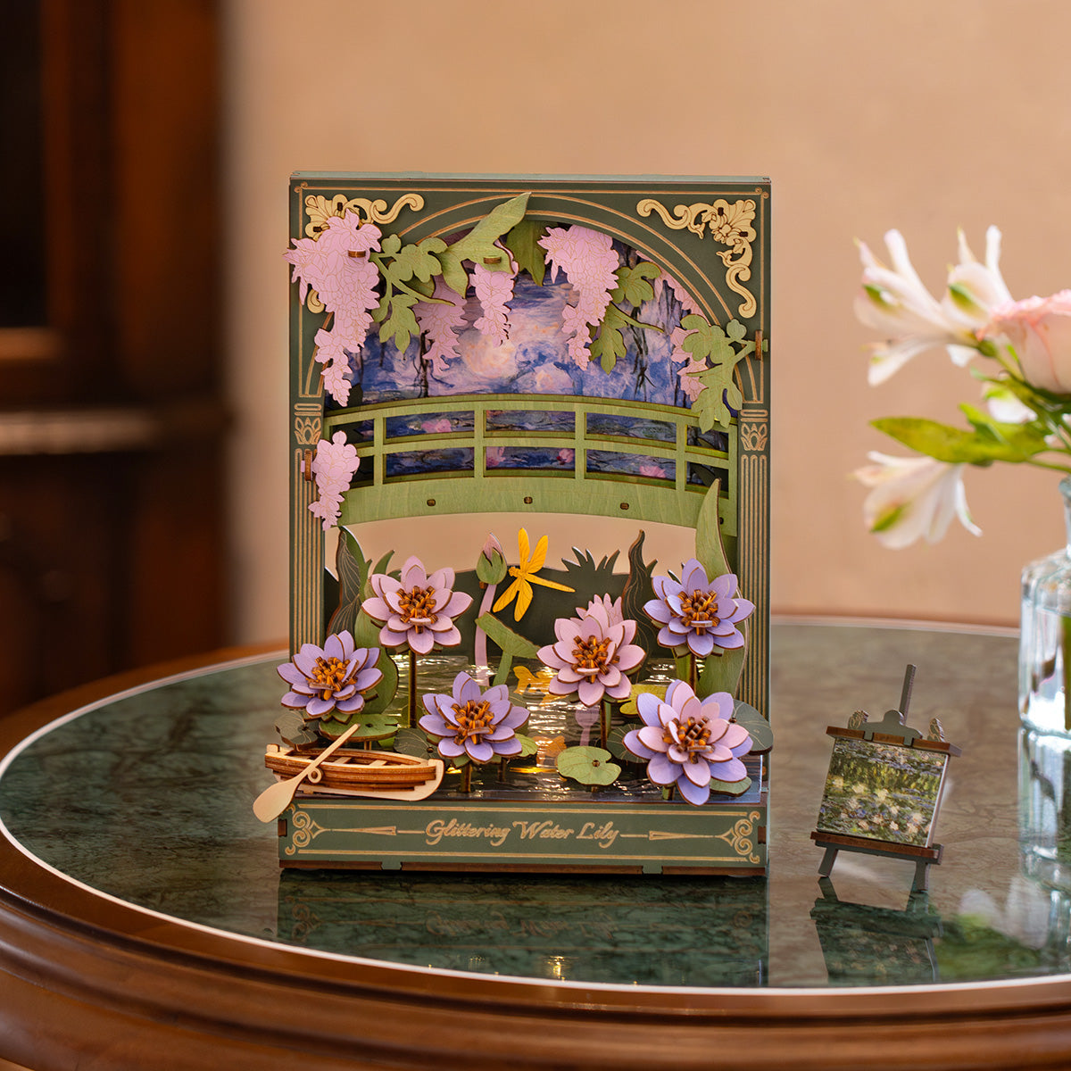 3D wooden craft model showing a pond scene with a green arched bridge, purple water lilies, and wisteria
