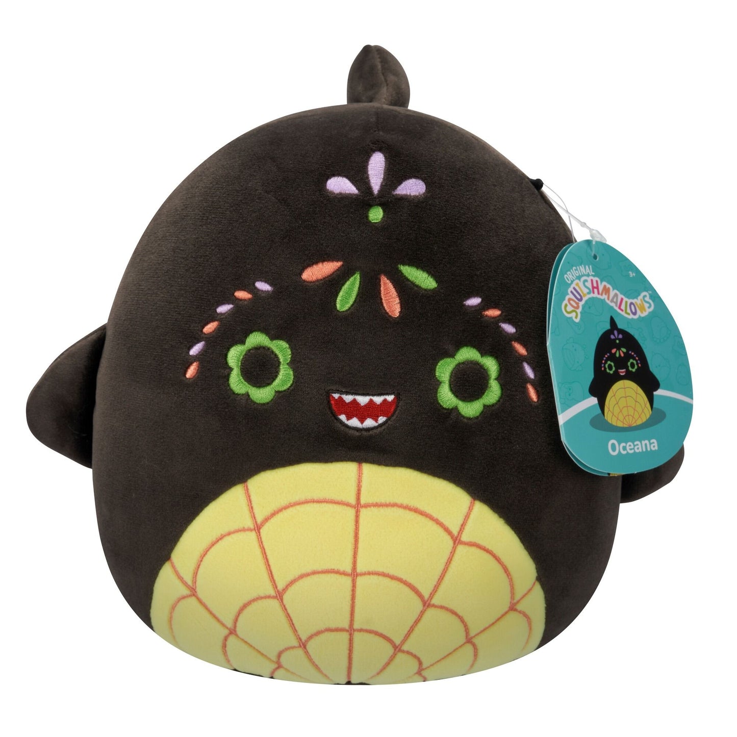 A dark brown plush toy with a sugar skull-inspired face, featuring green flower eyes, a red toothed mouth, colorful embroidery, a yellow web-patterned belly, and small fins