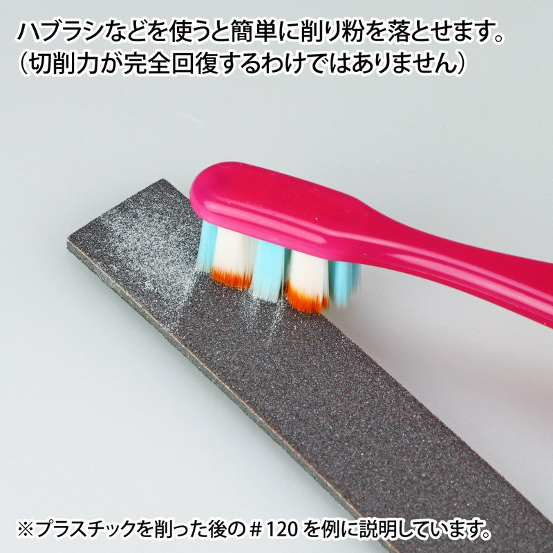 A pink toothbrush brushes white plastic dust from a dark sanding block