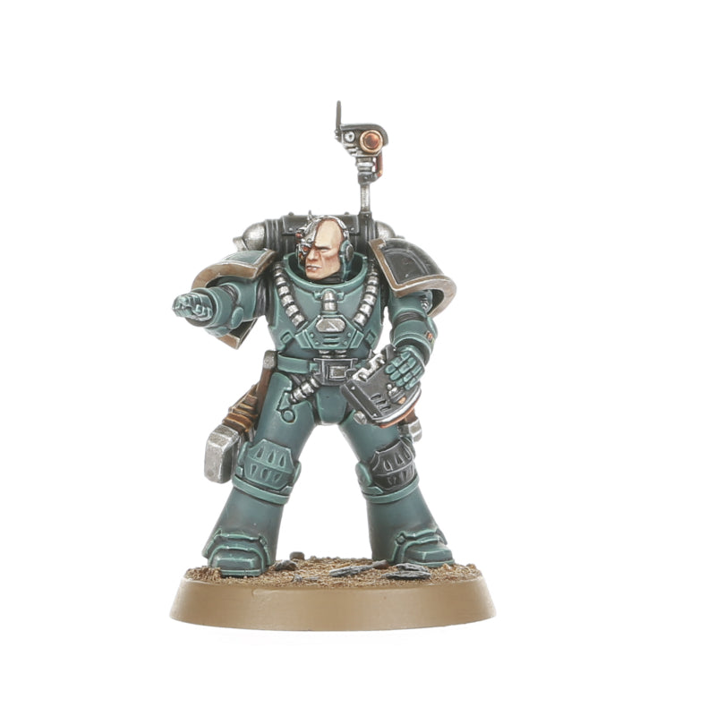 A miniature Space Marine figure in teal-grey power armor with a bionic head and backpack sensor array, pointing forward while holding a handheld device