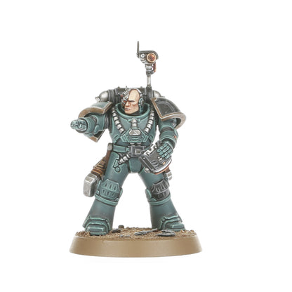 A miniature Space Marine figure in teal-grey power armor with a bionic head and backpack sensor array, pointing forward while holding a handheld device