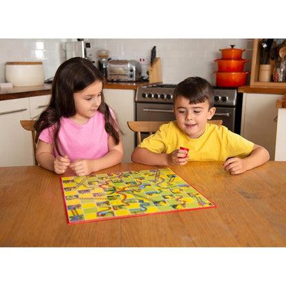 A girl and boy play the Snakes and Ladders and Ludo board game on a wooden table in a kitchen