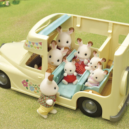 Six toy rabbit figures playing inside a yellow camper van that features a blue internal slide, set on green grass