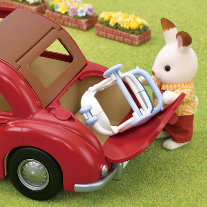 A bunny figure loading a blue and white baby seat into the open trunk of a red toy car on the grass