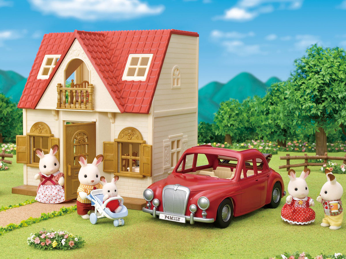 Five toy rabbit figures stand next to a red toy car and a two-story dollhouse with a red roof in a grassy yard