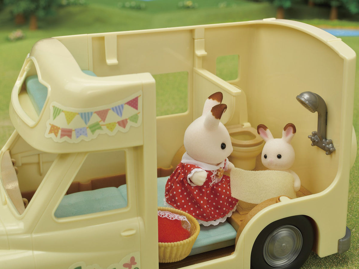 Toy rabbit adult drying a baby rabbit wrapped in a towel inside a beige toy camper