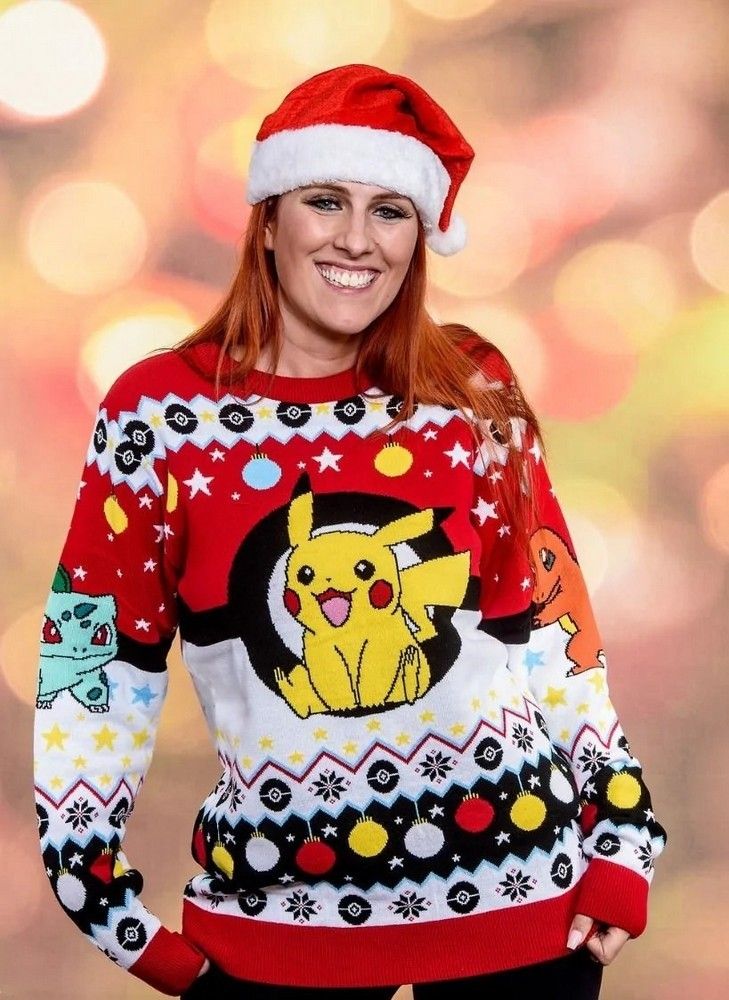 Smiling model in a Santa hat showcasing the red and white Pokemon Christmas Jumper with Pikachu centered in a Poké Ball, plus Bulbasaur and Charmander