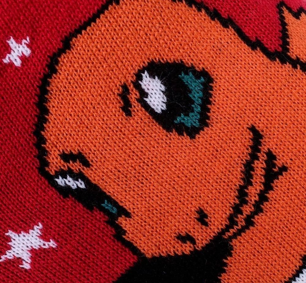 A close-up knit texture shot of the Pokemon Christmas Jumper highlighting the orange Charmander face and eye on a festive red fabric