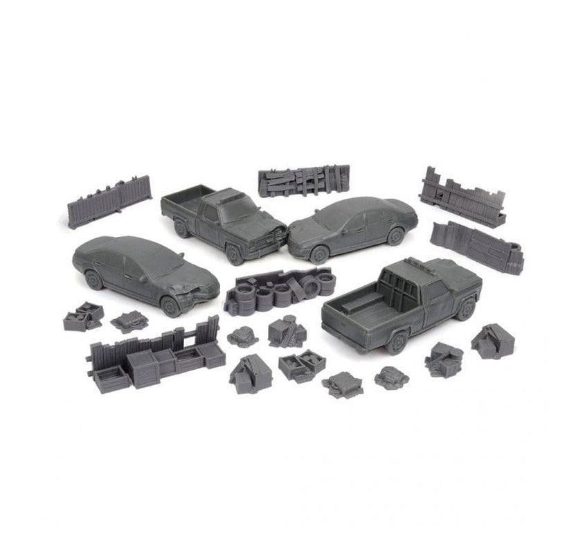 Unpainted gray miniature wargaming terrain: crashed cars, pickup trucks, barricades, barrels, tires, crates, and assorted debris