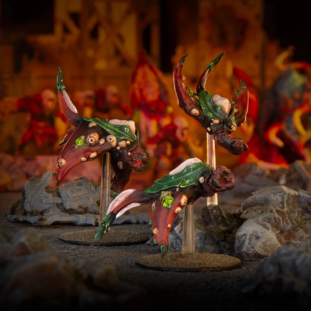 Three red and green multi-eyed flying Deadzone Nightmare Incursion Booster miniatures on clear stands over rocky terrain