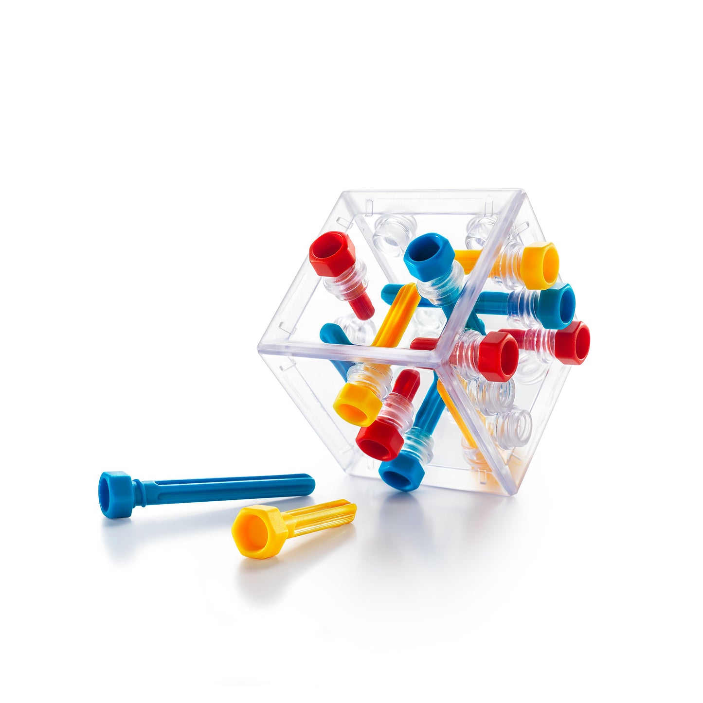 A transparent Criss Cross Cube puzzle housing interlocking red, blue, and yellow plastic pegs, with two loose pieces on the white surface