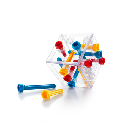 A transparent Criss Cross Cube puzzle housing interlocking red, blue, and yellow plastic pegs, with two loose pieces on the white surface