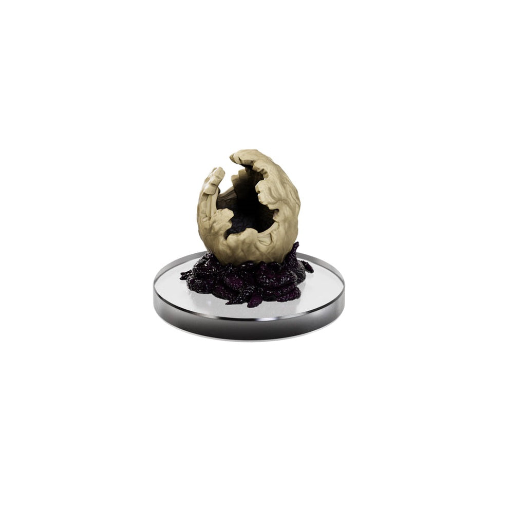 Cracked beige pod resting on dark purple residue on a round, mirrored display base