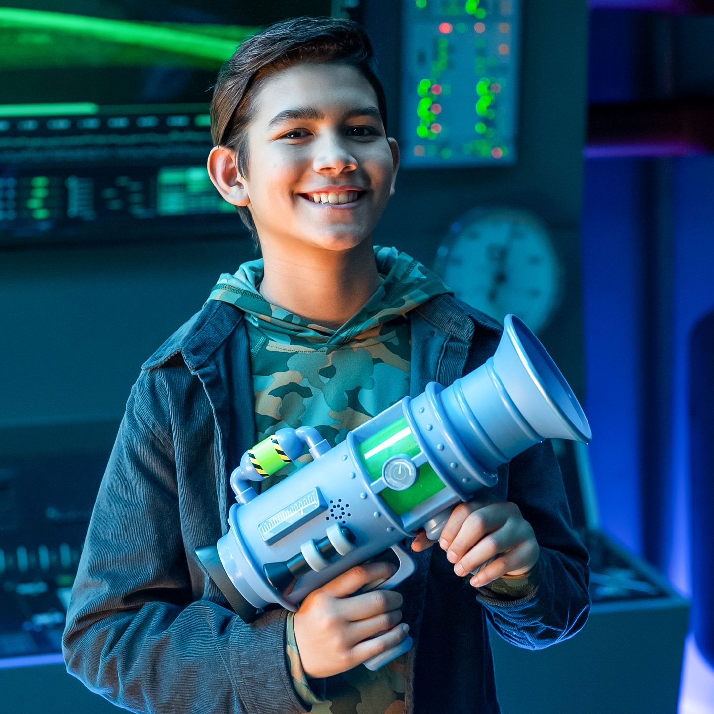 A happy boy holds the light blue and green Moose Despicable Me 4 Ultimate Fart Blaster, featuring a large flared end, a power dial, and hazard stripes, set in a sci-fi room
