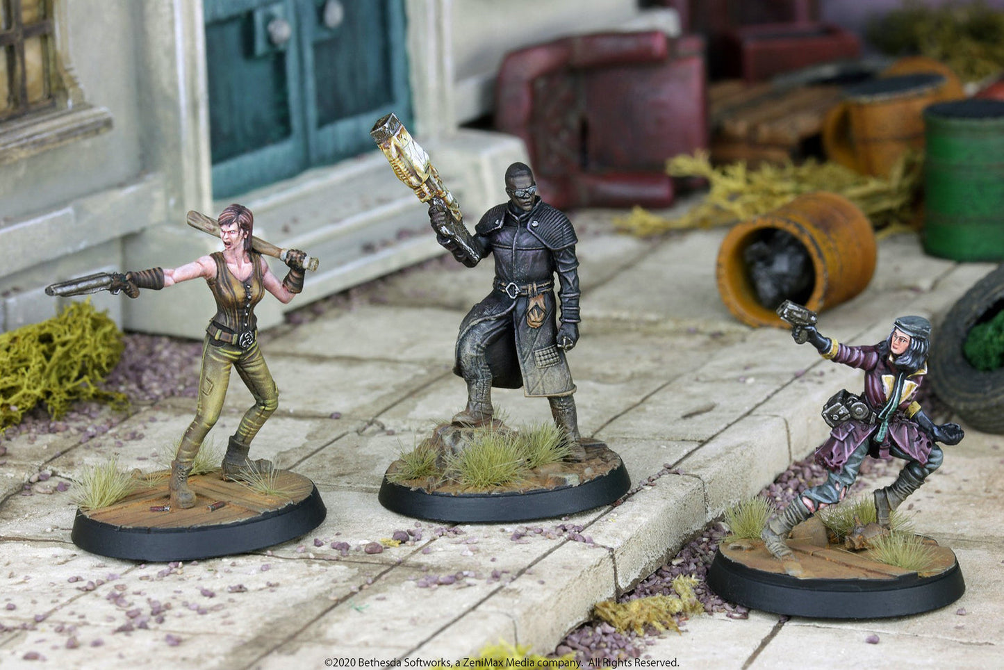 Three Fallout miniatures: a woman with a pistol/bat, a man with a large gun, and a woman aiming a pistol, posed in a ruined city.