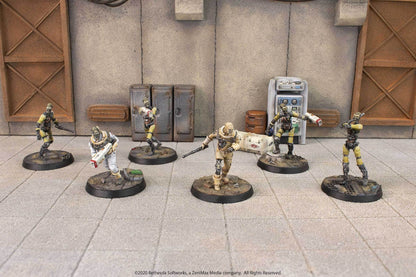 Six armed, ghoulish Fallout miniatures in a post-apocalyptic industrial scene, one wearing a white hazmat suit