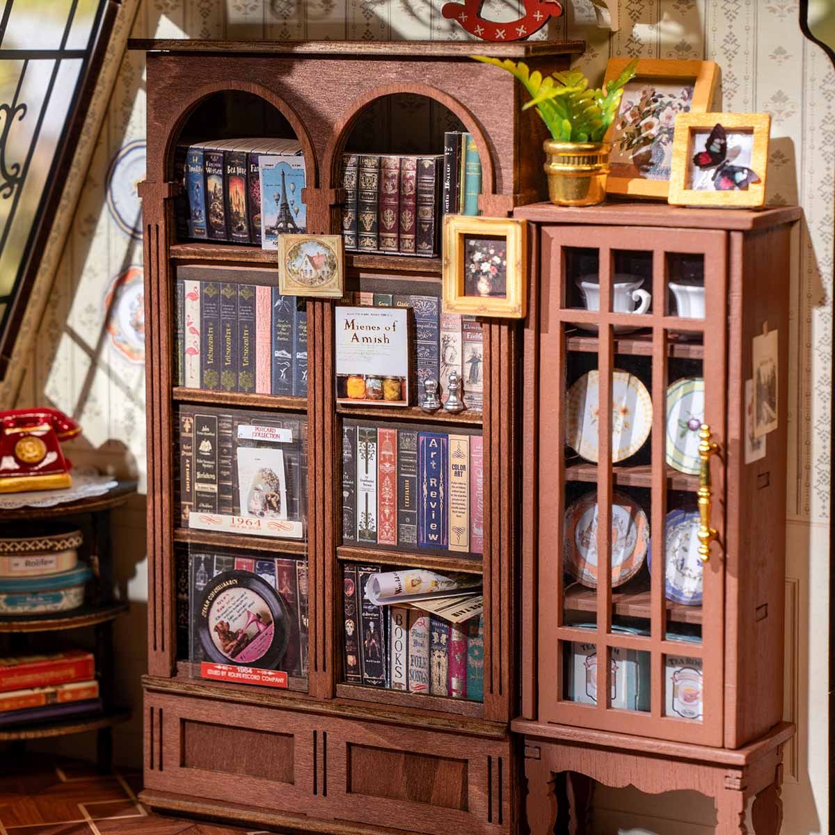 Detailed miniature scene featuring a wooden bookshelf packed with tiny books and an adjacent china cabinet