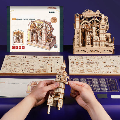 Hands assembling a detailed wooden 3D puzzle model of Big Ben, with the finished London kit displayed