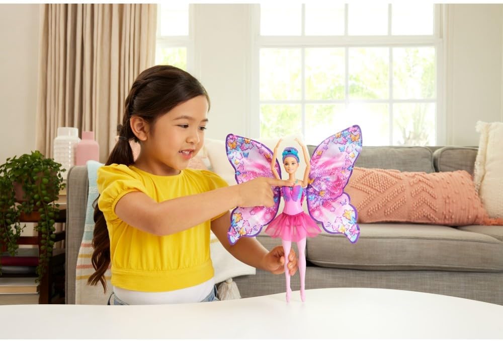 Smiling girl points at a pink ballerina fairy doll with large butterfly wings