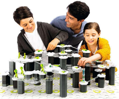 Three people smiling, building a complex multi-level marble run toy