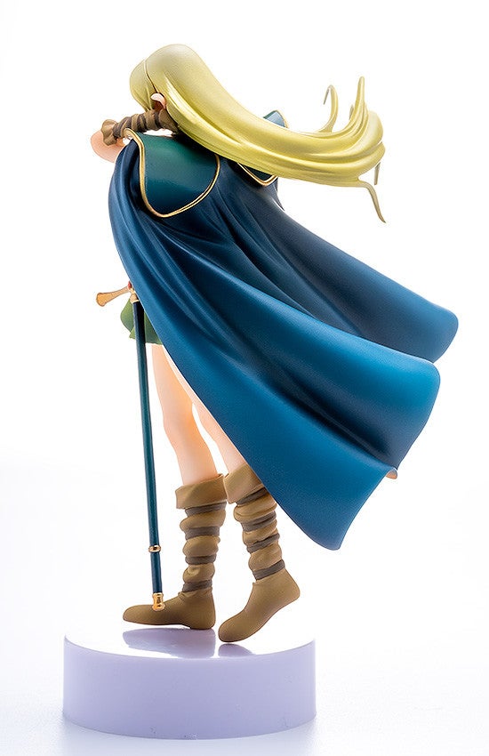 Anime figure with blonde hair blue cape green clothing and tan boots holding a staff