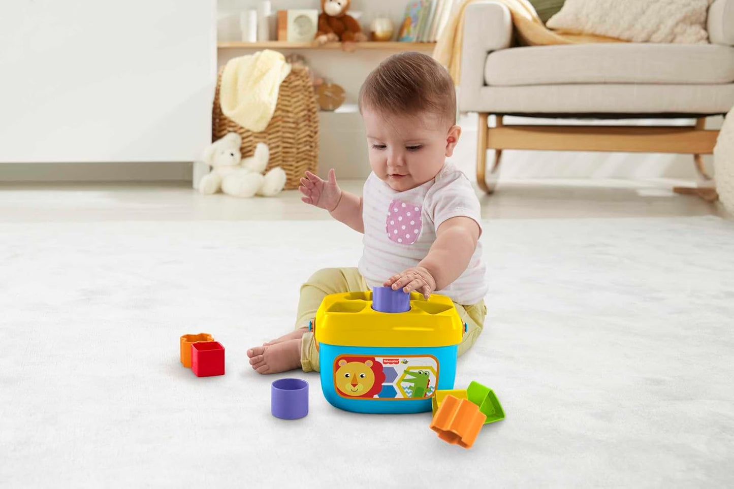 Baby sits on a white rug -  placing a purple block into a yellow and blue shape sorter toy