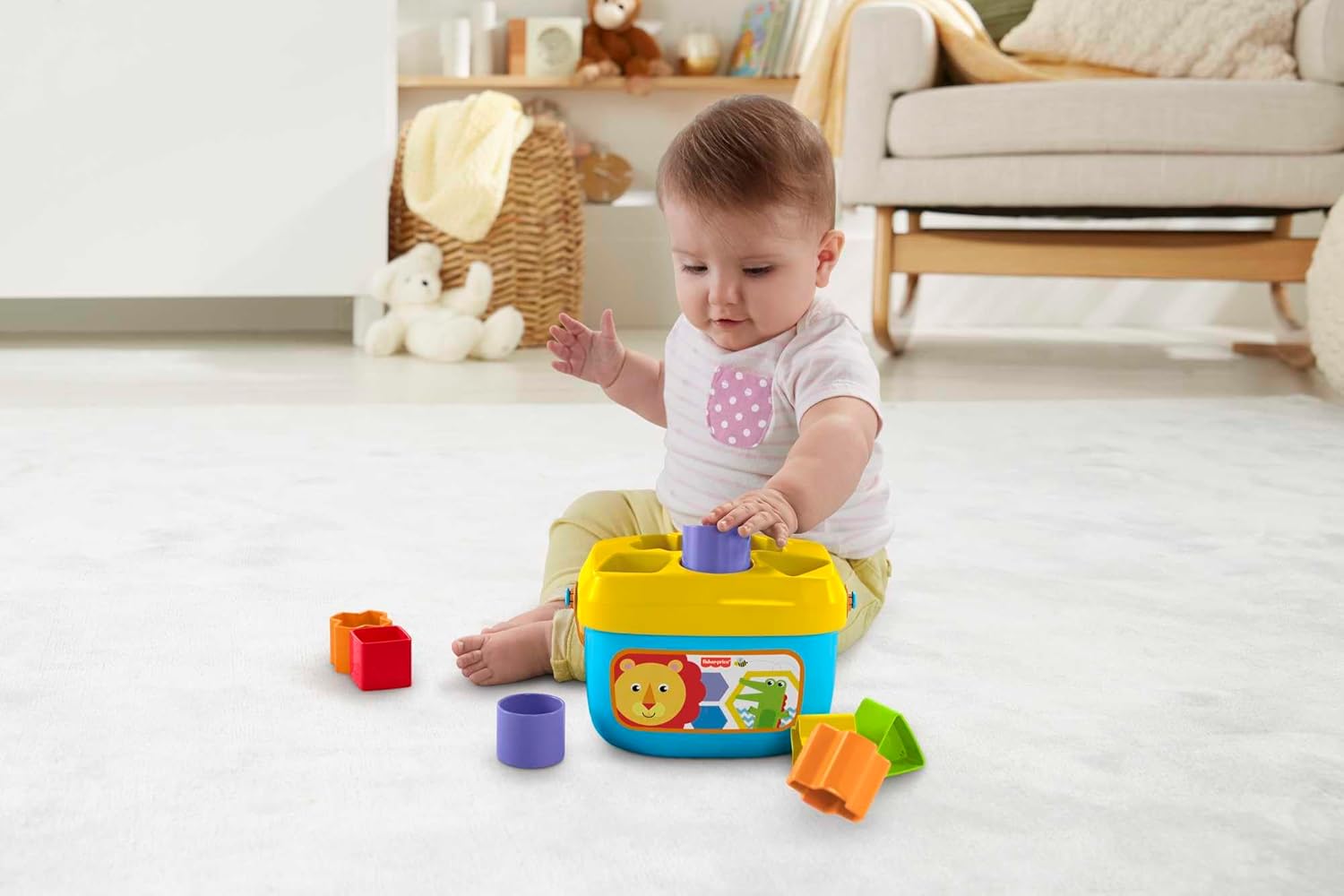 Baby sits on a white rug -  placing a purple block into a yellow and blue shape sorter toy