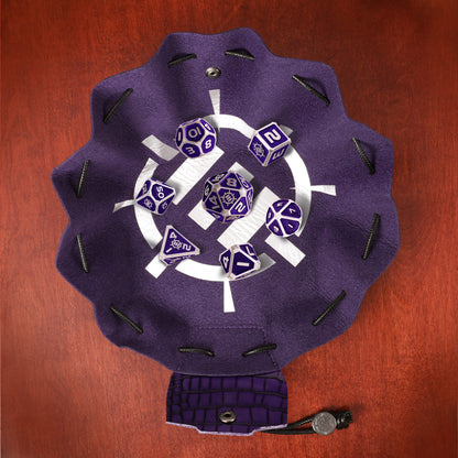 A purple 2-in-1 Vegan Leather Bag and Tray, featuring a white symbol, holds a Tabletop Collector's Metal RPG Dice Set in purple and silver, along with a snap closure and token on wood