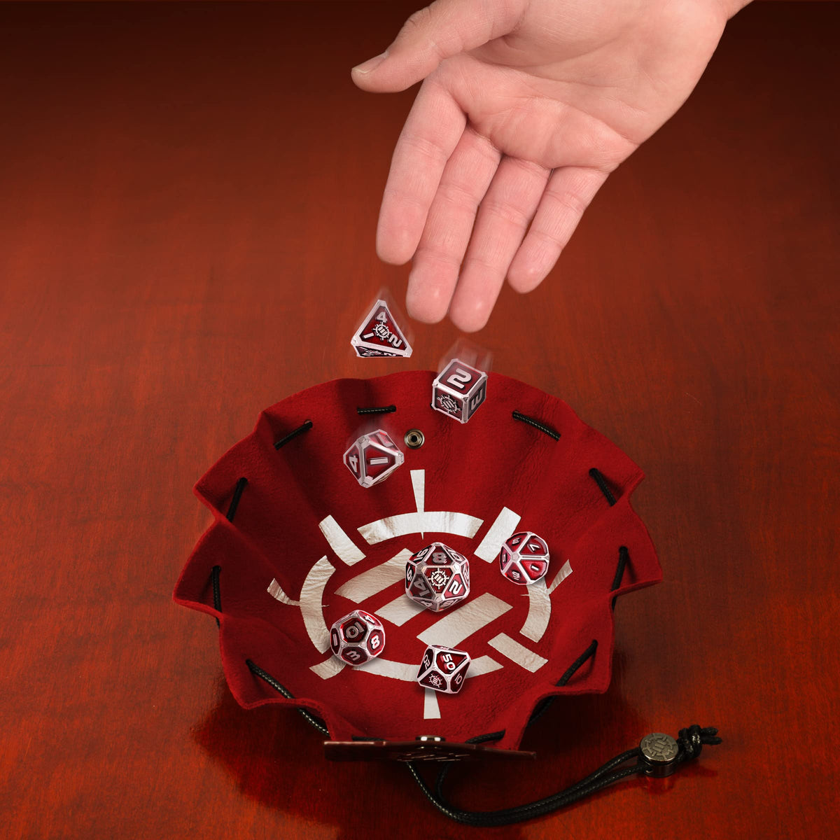 A hand drops silver and red metal RPG dice into the red vegan leather bag and tray from the Enhance Tabletop Collector&#39;s Metal RPG Dice Set