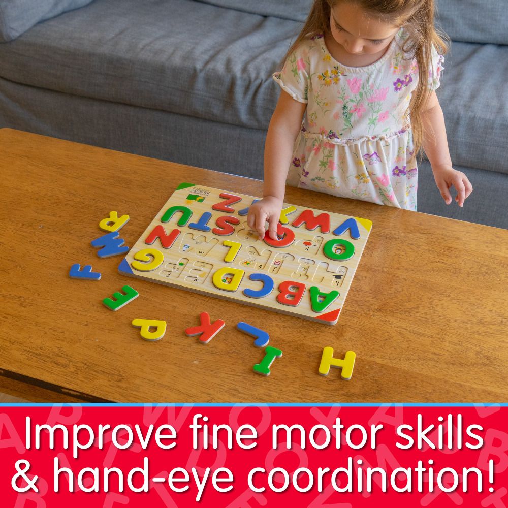Young child playing with a colourful wooden alphabet letter puzzle on a wooden table, focusing on putting in the letter R