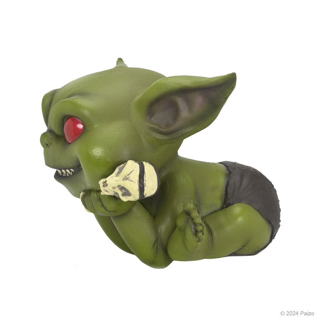 Green baby goblin with red eyes, sharp teeth, and black diaper, holding a small skull, resting its head