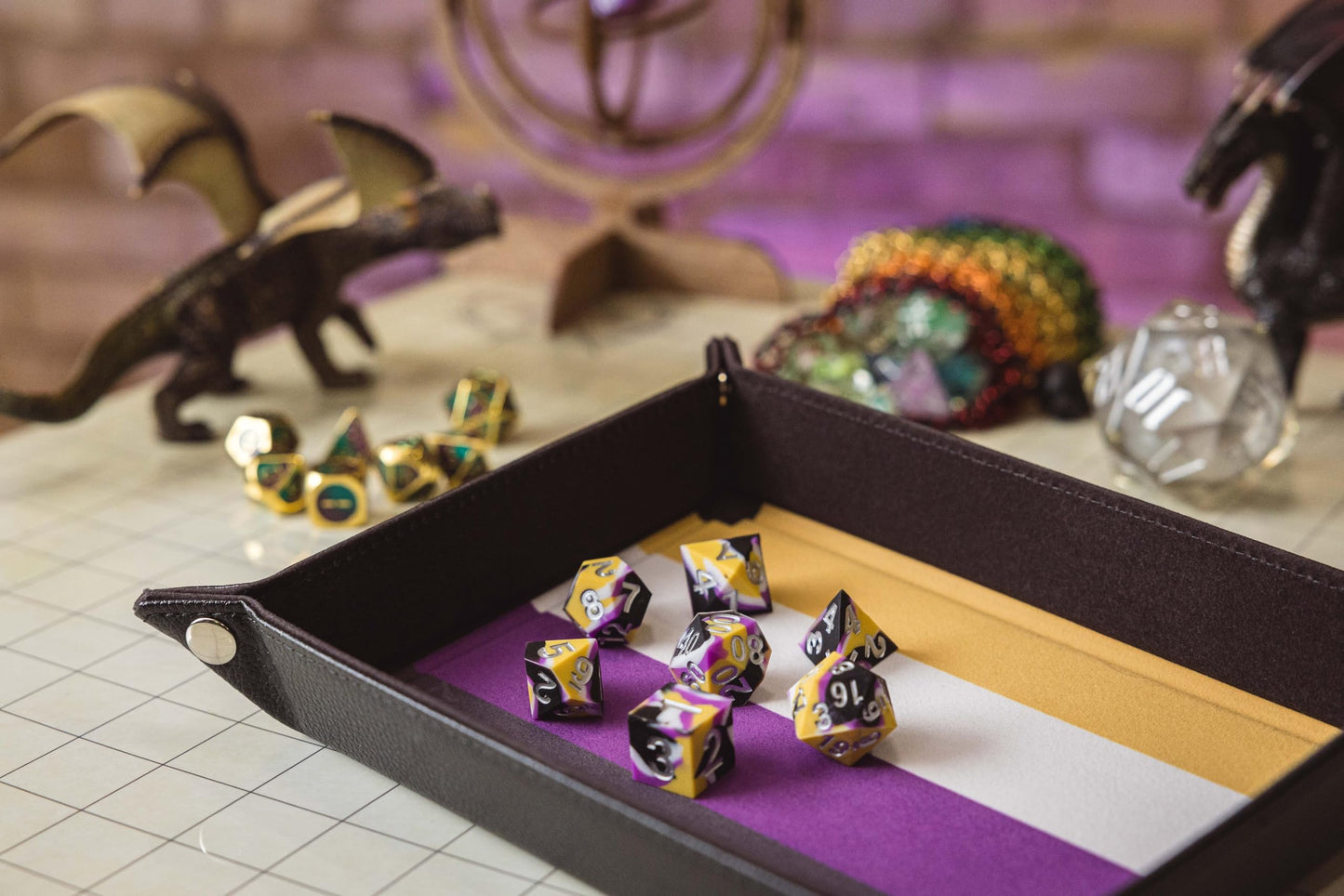 The Nonbinary Pride fold-up dice tray features a purple white and yellow striped velvet interior filled with matching polyhedral dice and surrounded by fantasy decor